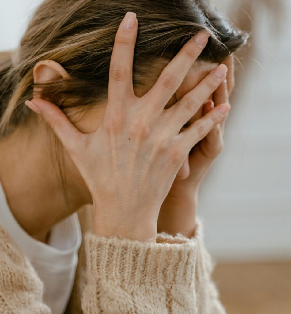 pexels-photo-7699410-7699410 Woman sitting indoors with face covered by hands, expressing stress and frustration.