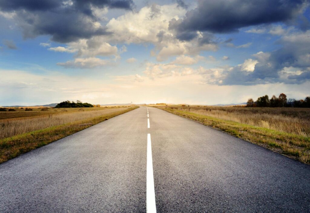 road-asphalt-space-sky-56832-56832 A long straight road stretches through fields under a dramatic cloudy sky.